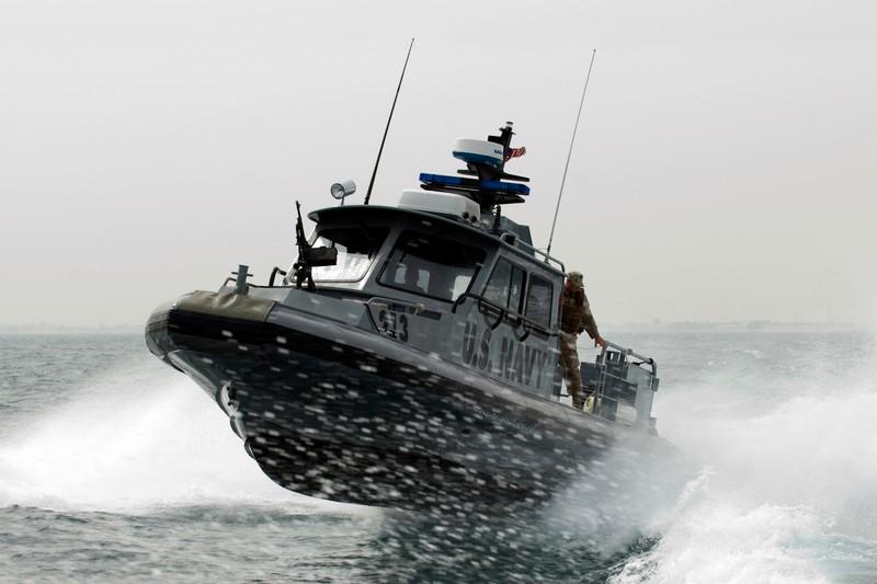 A military patrol boat cuts through rough waters near Kuwait Naval Base under an overcast sky