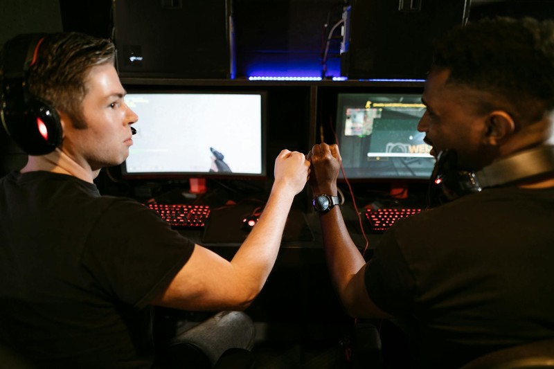 Two gamers fist bumping at a PC gaming station with monitors and backlit keyboards