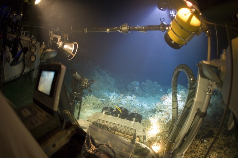 View from inside a submersible showing underwater equipment and the ocean floor with coral formations