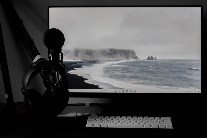 A dimly lit gaming desk setup with a monitor, microphone, headphones, and keyboard