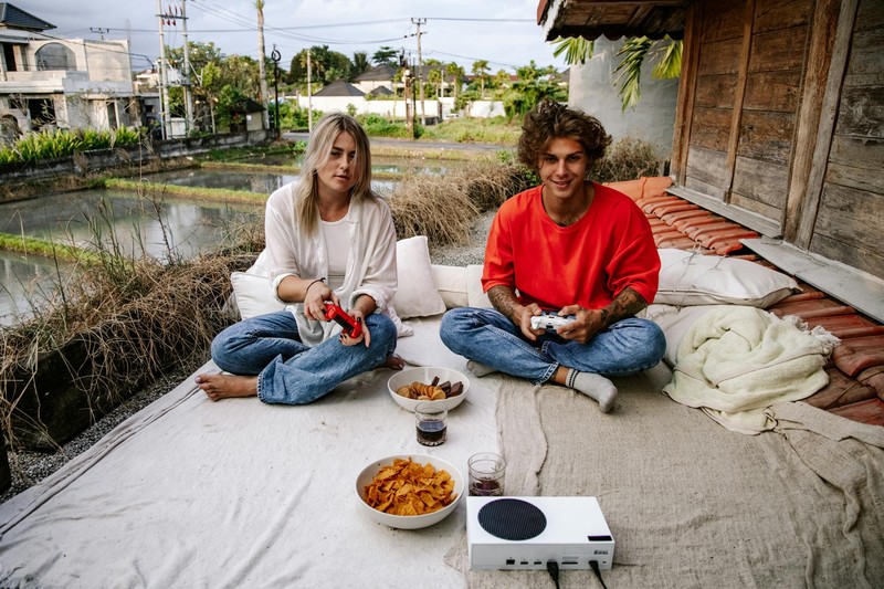 Two friends playing video games together on an outdoor rooftop terrace with snacks and game controllers