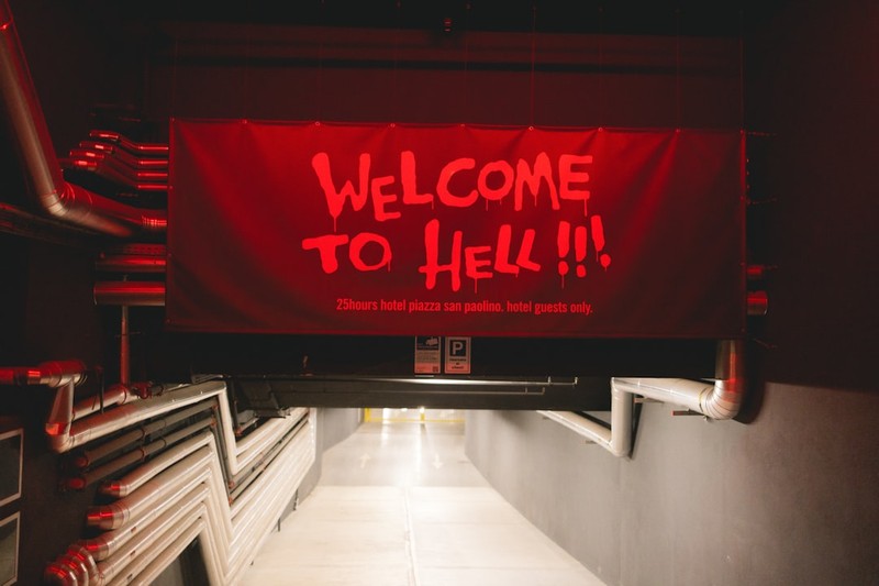A red sign reading Welcome to Hell hangs in a dimly lit industrial corridor