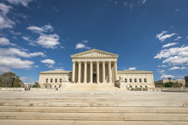 The United States Supreme Court building in Washington, D.C., under a clear blue sky with scattered clouds