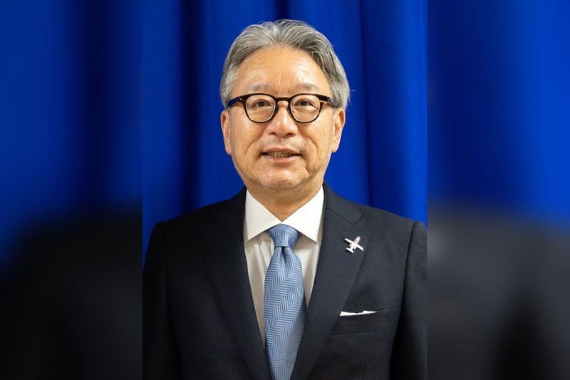 Formal portrait of Honda CEO Toshihiro Mibe wearing a dark suit and glasses against a blue backdrop