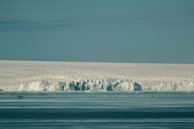 A massive Antarctic ice shelf meets calm turquoise waters under a clear blue sky