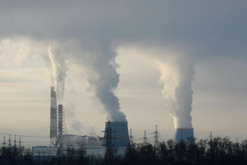 Industrial smokestacks and cooling towers billowing thick smoke and steam into an overcast sky