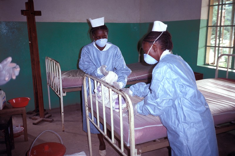 Two nurses in protective gowns and masks attending to patients in an Ebola isolation ward at Kikwit General Hospital, 1995