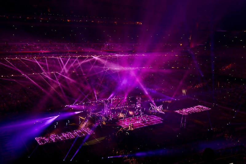 Aerial view of a Super Bowl halftime show stage with dramatic purple and pink lighting filling a packed stadium