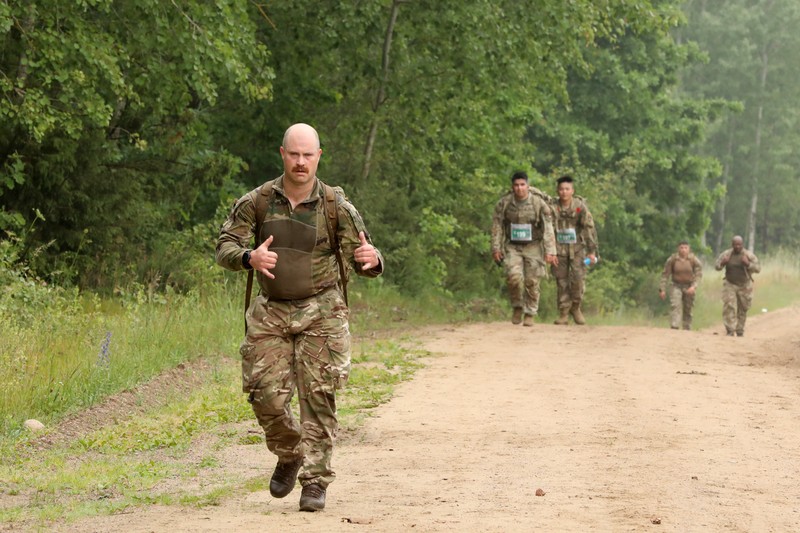 Multinational NATO troops running along a dirt path during training exercises in a wooded area in Poland