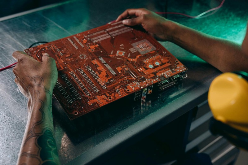 A technician's hands working on a printed circuit board with a soldering tool in an industrial setting