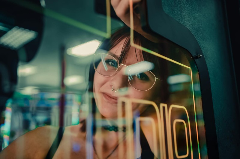 A woman reflected in arcade machine glass enveloped in vibrant neon lights