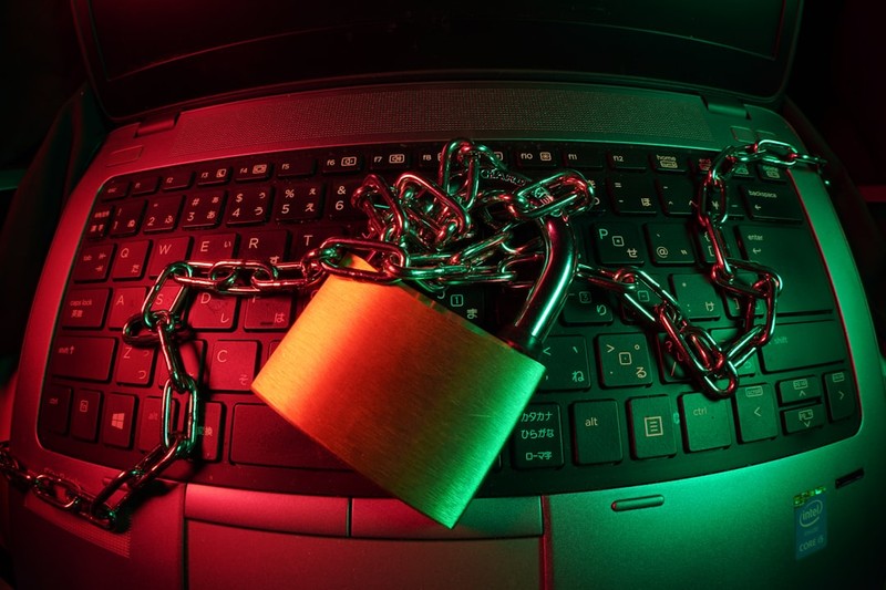 A gold padlock and metal chains secured across a laptop keyboard under dramatic red and green lighting