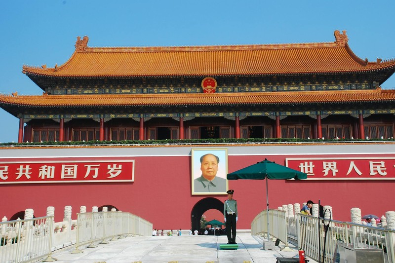 Tiananmen Gate in Beijing with Mao Zedong portrait, red flags, and banners under an overcast sky