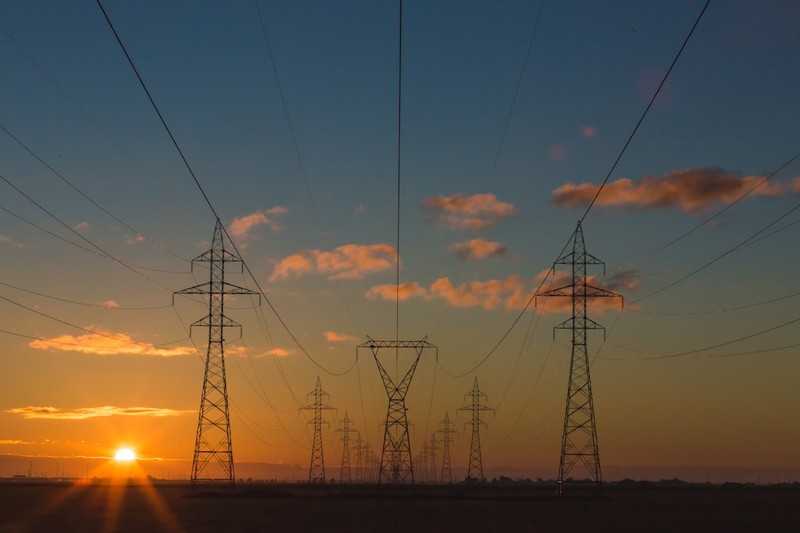 High-voltage power transmission towers silhouetted against a vibrant sunset sky