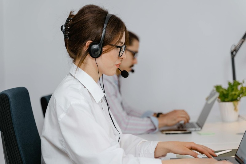 Two customer service agents wearing headsets working at computers in a call center office