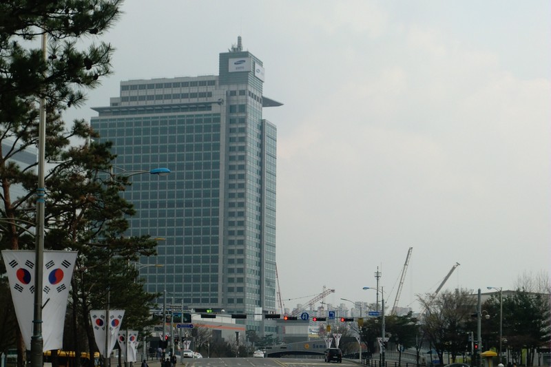 Samsung Electronics headquarters building in Suwon, South Korea, with the South Korean flag visible in the foreground.
