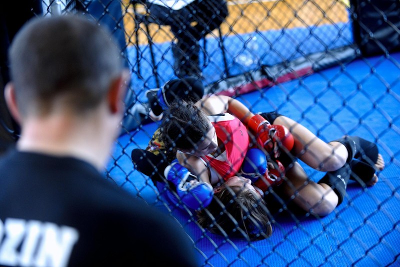 Two women grappling on the mat inside an MMA cage during a fight