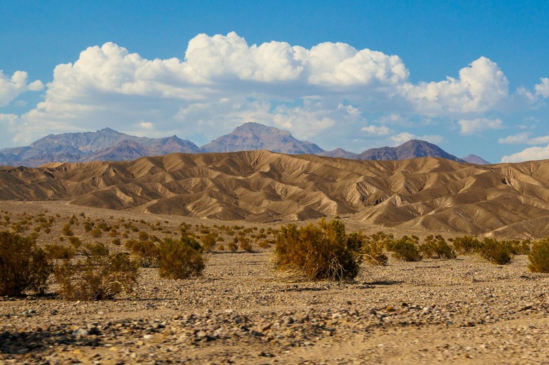 Rugged desert terrain with rolling hills and distant mountains under a blue sky in Furnace Creek, Death Valley, California