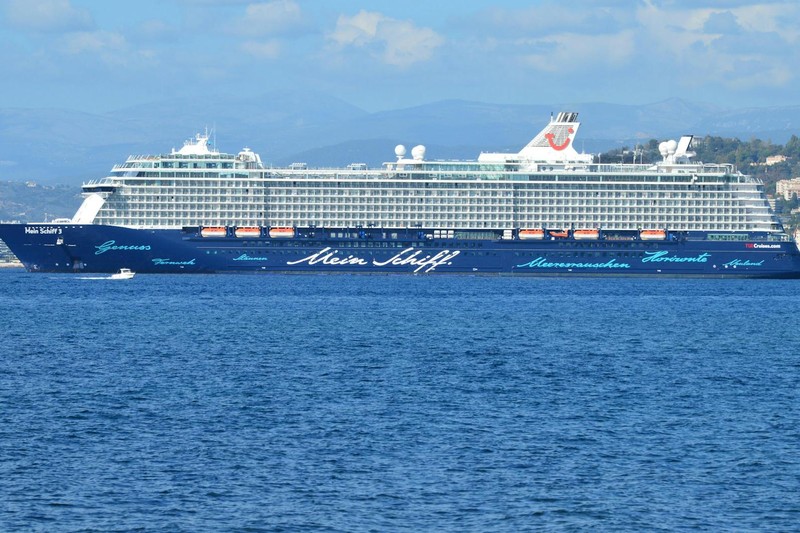 A large cruise ship sails across the open ocean under a partly cloudy sky