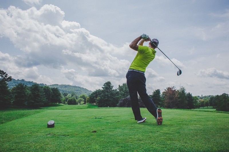 A golfer in a green polo shirt follows through on a swing at a tee box under a cloudy sky