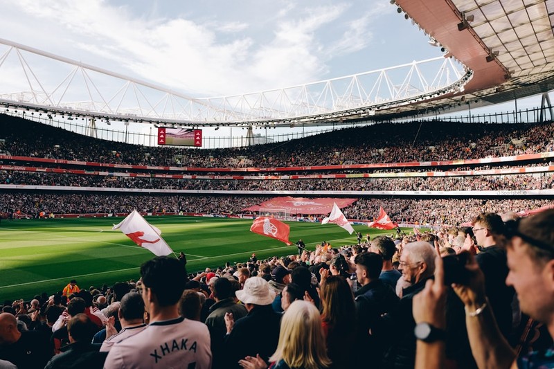 Arsenal fans pack Emirates Stadium during a home match, with red and white flags visible across the stands and pitch