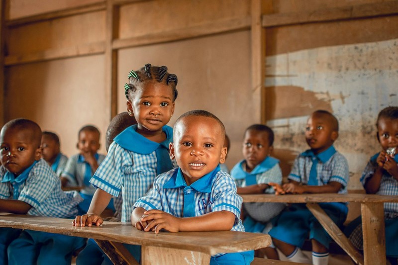 Children seated at wooden desks in a Nigerian classroom wearing blue-and-white school uniforms