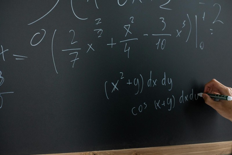 A hand writing mathematical equations on a blackboard