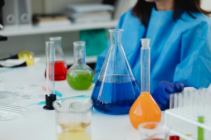 Colorful chemical solutions in glassware on a laboratory bench with a researcher in protective gear