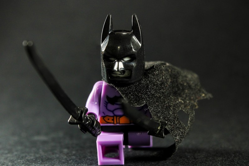 LEGO Batman minifigure in a dynamic action pose holding a sword against a dark background