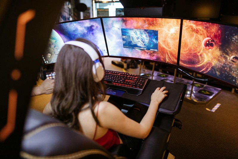 A person in a gaming chair using a multi-monitor PC gaming setup with keyboard and mouse