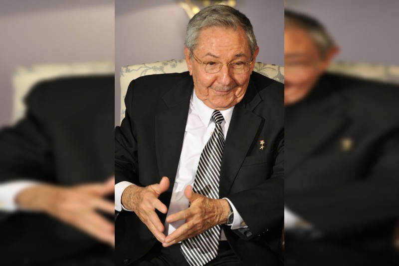 Formal portrait of Raúl Castro in a black suit and striped tie, wearing glasses, seated in an official setting.