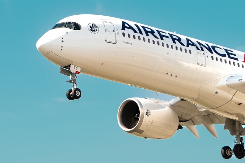 An Air France wide-body jet flying through a clear blue sky with landing gear extended