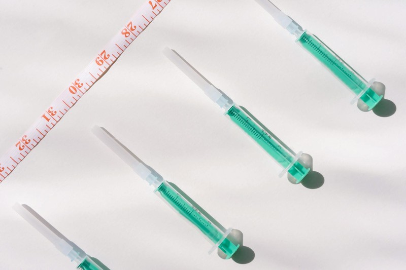 Green-filled syringes and an orange measuring tape arranged on a white background