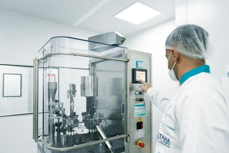 A worker in protective gear operates machinery on a pharmaceutical production line in a sterile cleanroom