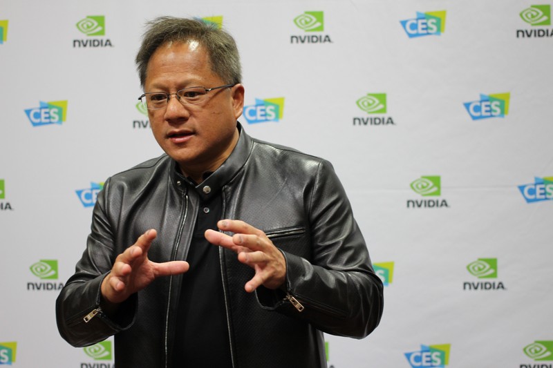 Nvidia CEO Jensen Huang gesturing while speaking at a CES event with Nvidia branding in the background