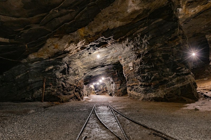 An illuminated underground mine tunnel with railroad tracks receding into darkness