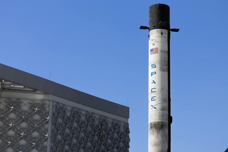 A SpaceX Falcon 9 rocket standing vertically outdoors against a clear blue sky, with soot marks showing prior launches