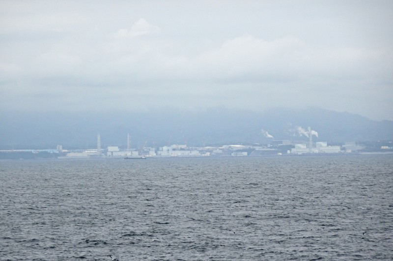 The Kashiwazaki-Kariwa Nuclear Power Plant viewed from the sea with mountains rising behind it under overcast skies