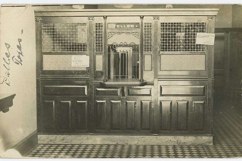 Historical bank teller window with a prominent TELLER sign in a black-and-white photograph from early 1900s Dallas, Texas