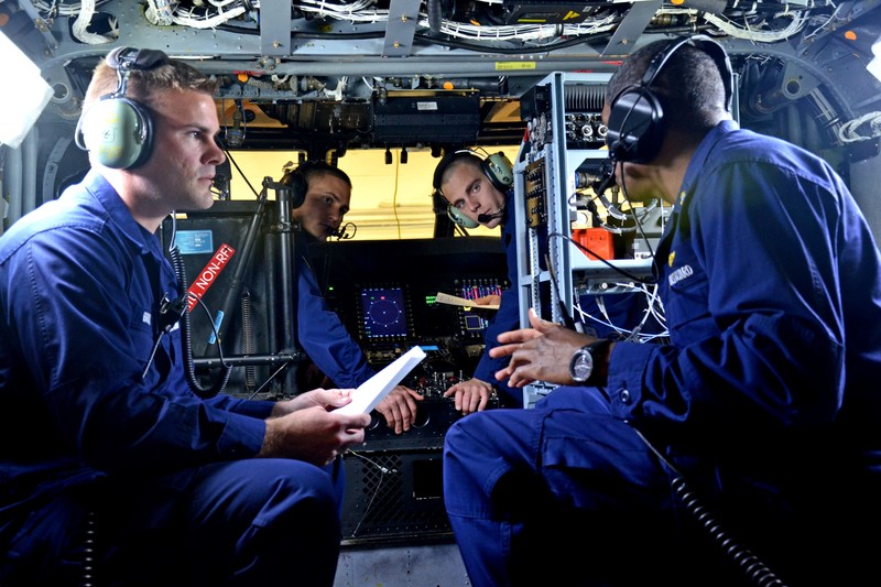 Aviation electronics technicians in a Coast Guard aircraft reviewing procedures with headsets and equipment