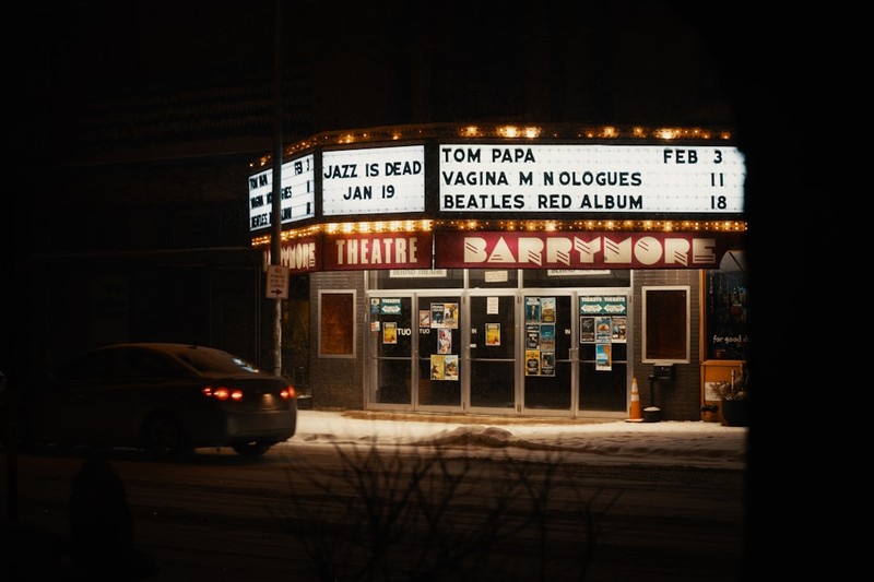 A theater marquee lit up at night with snow on the ground, displaying upcoming show listings