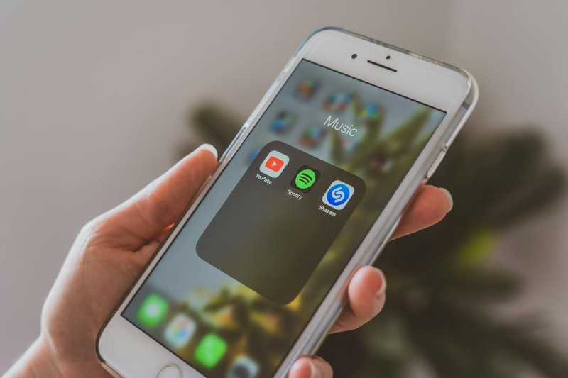 A person's hand holding a smartphone displaying the Spotify app alongside other music apps