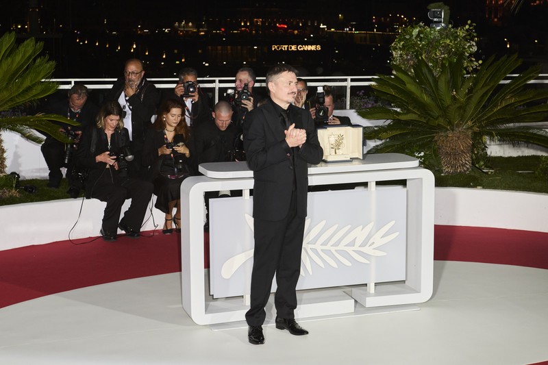 Cristian Mungiu stands at a podium at the Cannes Film Festival with the Palme d'Or trophy