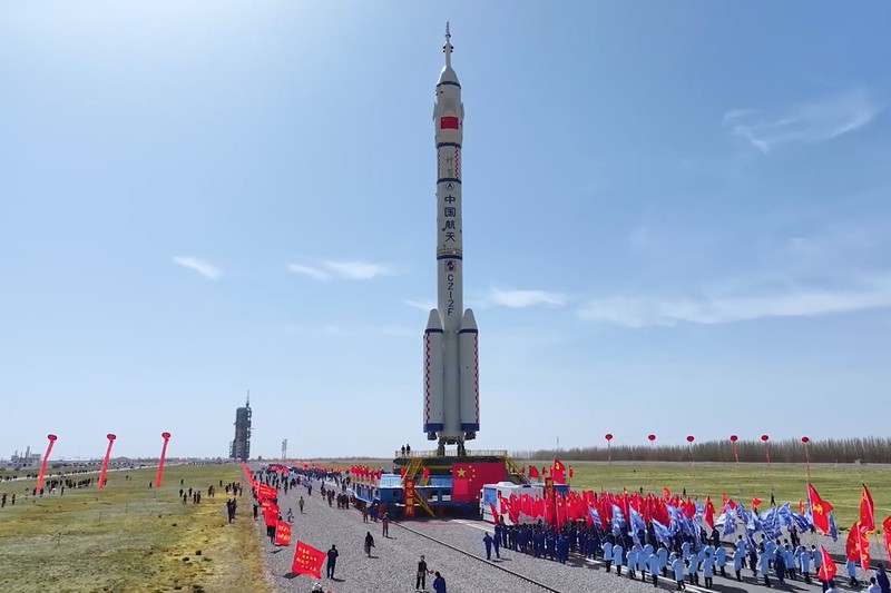 A Long March rocket on its mobile launch platform during rollout at a Chinese spaceport, surrounded by a crowd holding flags