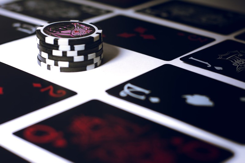 A stack of black-and-white poker chips surrounded by playing cards on a white surface