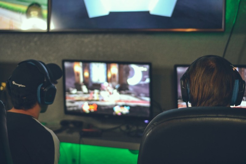 Two gamers sitting side by side at monitors playing a cooperative PC game together
