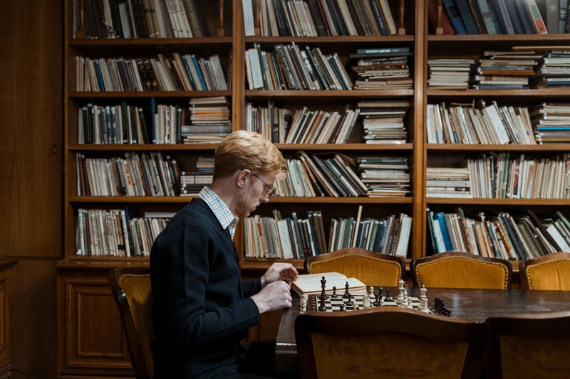 A person focused on a game in a warm, book-filled library with wooden shelves