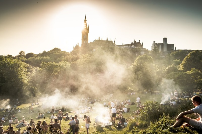 Crowds of people enjoying sunshine in a British park with a historic building visible in the background
