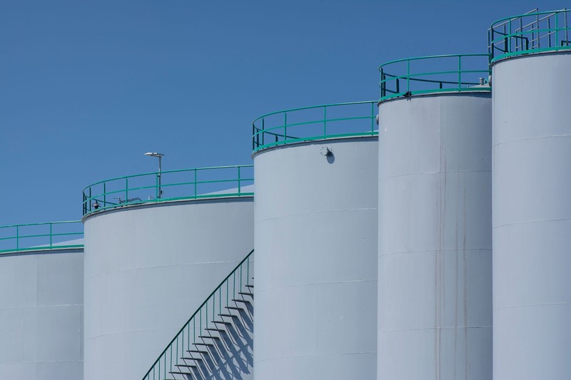 Large white cylindrical industrial storage tanks with green safety railings under a clear blue sky
