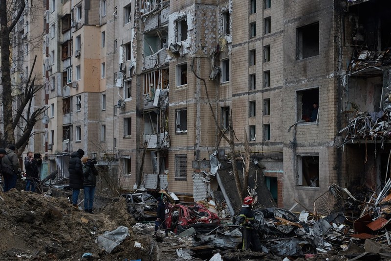 Heavily damaged multi-story residential building in Kyiv following a Russian missile strike, with debris scattered below and onlookers nearby